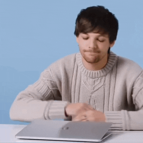 a man in a sweater is sitting at a table using a laptop computer .