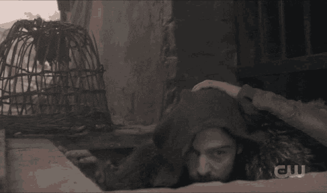 a man in a fur coat is reaching out from behind a wall with the letters cw on the bottom
