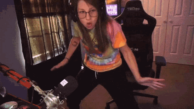 a woman in a tie dye shirt is dancing in front of a techin chair