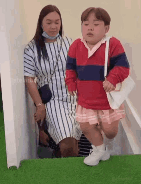 a woman is sitting next to a little boy wearing a striped dress and a red sweater .