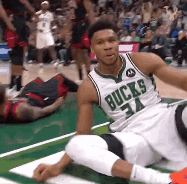 a basketball player wearing a bucks jersey is sitting on the court
