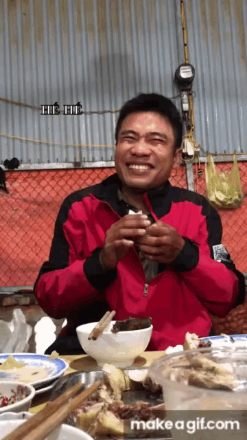 a man in a red jacket is sitting at a table with bowls of food and plates of food