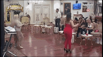 a woman in a red jumpsuit is dancing in front of a group of people in a living room with the word parovi on the screen
