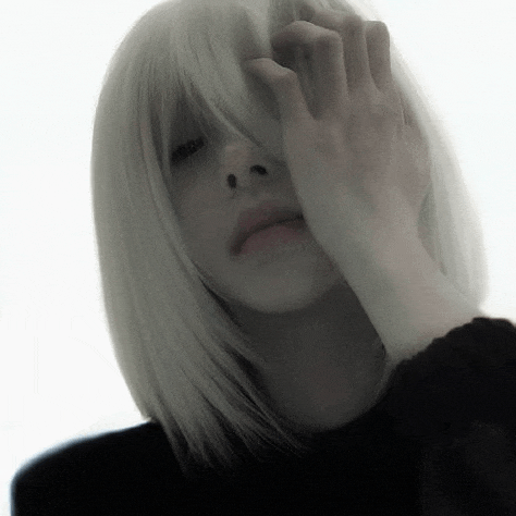 a woman with white hair is covering her face with her hand and wearing a black sweater .