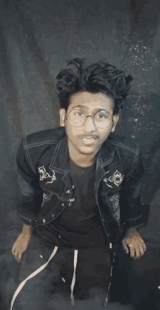 a young man wearing glasses and a denim jacket