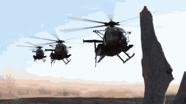 three military helicopters are flying in formation over a desert landscape