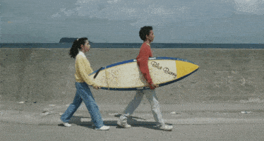 a man and woman carrying a surfboard that says blue berry on it