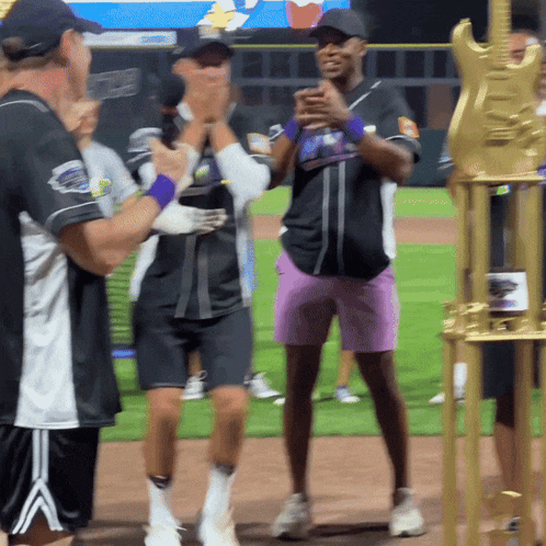 a group of people are standing on a baseball field with a trophy in the foreground
