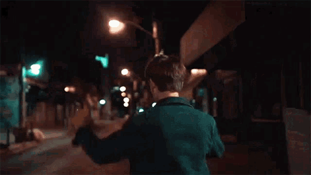 a man in a blue jacket is walking down a city street at night .