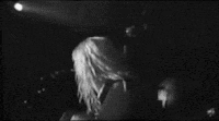 a black and white photo of a woman standing in front of a microphone on a stage .