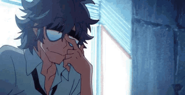a man wearing glasses is sitting in front of a window with his hand on his nose .