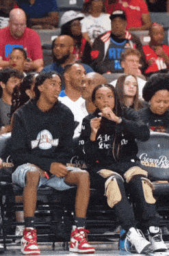 a group of people sitting in a stadium with one wearing a black sweatshirt that says atl deep tech
