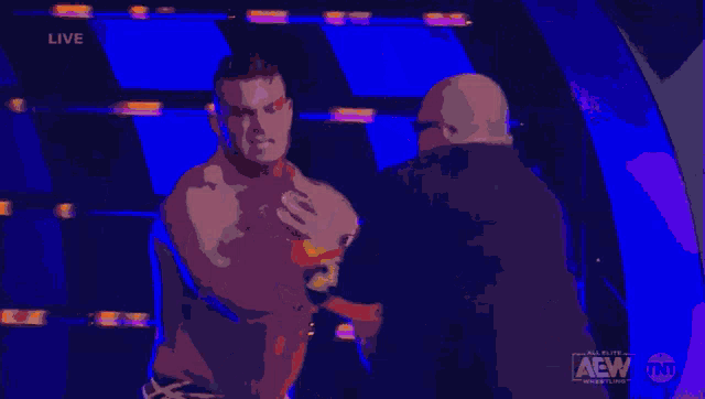 a shirtless wrestler is being interviewed by a man with a tnt logo on the bottom right