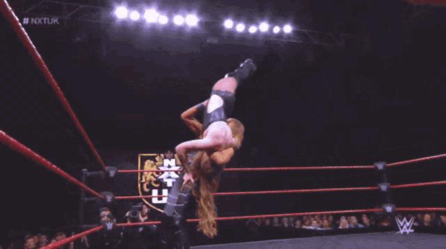 two women are wrestling in a ring with the nxt uk logo on the wall behind them