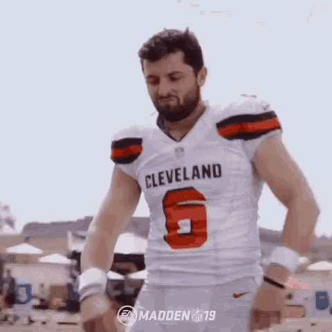 a man in a cleveland browns jersey is standing on a beach with his arms outstretched .
