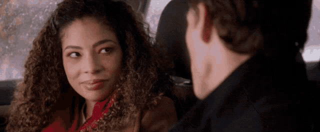 a woman with curly hair is sitting in the back seat of a car talking to a man
