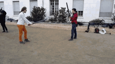 a man in orange pants is holding a sword while another man holds a bat