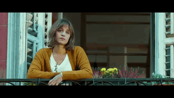 a woman in a yellow sweater stands on a balcony