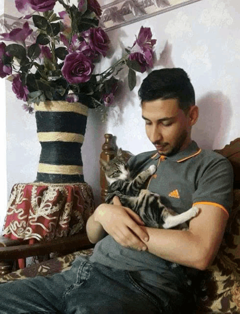 a man in an adidas shirt holds a cat in his lap