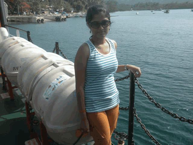 a woman in a striped tank top leans against a railing in front of a boat with a life preserver on it
