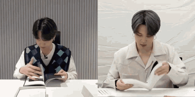 two men are sitting at a table reading books . one is wearing a vest and the other is wearing a white shirt .