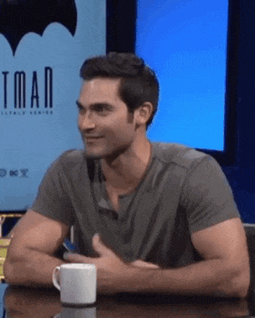 a man is sitting at a table with a cup of coffee in front of a batman sign .