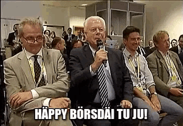 a man in a suit is holding a microphone in front of a crowd and says happy borsdai tu ju !