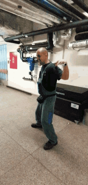 a man in overalls is standing in a hallway with pipes behind him and a sign that says fire exit