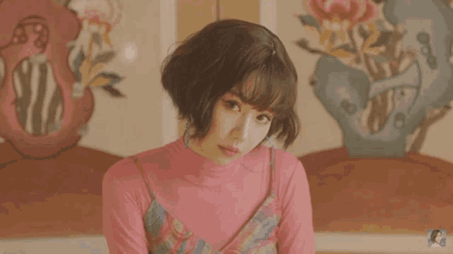 a woman with short hair and bangs is wearing a pink top and a plaid dress .