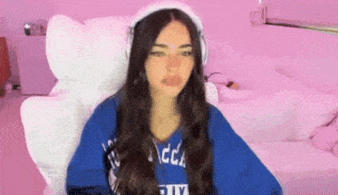 a woman wearing headphones and a blue shirt is sitting in a chair in front of a pink wall .