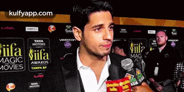 a man in a suit is holding a bag of chips in front of a sign that says iifa magic movies