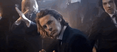 a man in a suit and tie is standing in front of a group of people in a dark room .