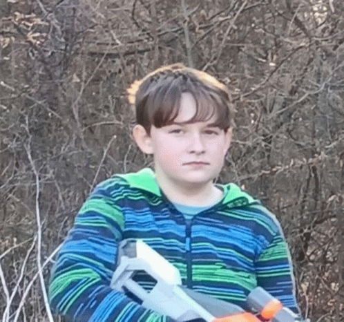 a young boy in a blue and green striped shirt is holding a toy gun .