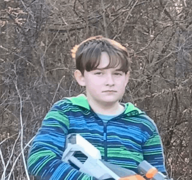 a young boy in a blue and green striped shirt is holding a toy gun .
