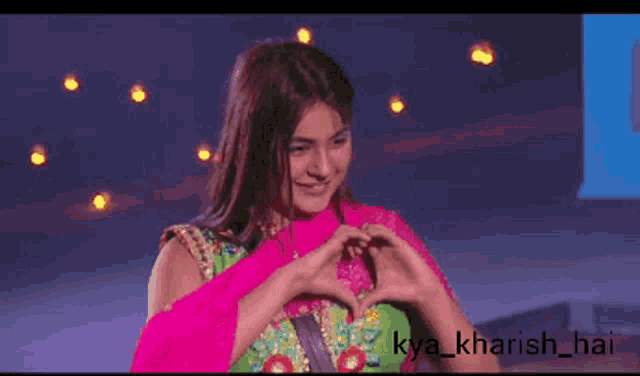 a woman is making a heart shape with her hands and the caption kya_kharish_hai is below her