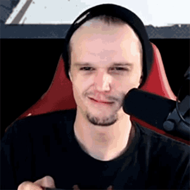 a man wearing a beanie and a black shirt is sitting in a red chair in front of a microphone .