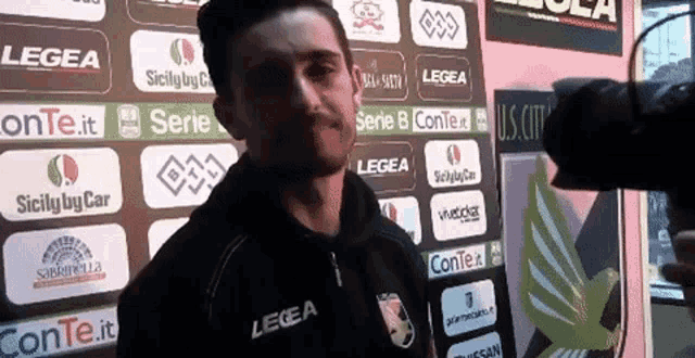 a man wearing a legea jacket stands in front of a sign that says serie b