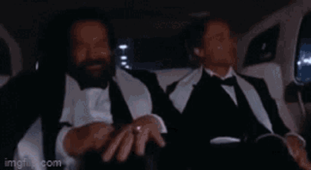 two men in tuxedos and bow ties are sitting in the back seat of a limousine .