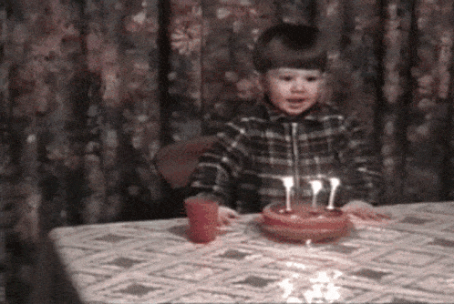 a little boy is sitting at a table with a birthday cake and candles