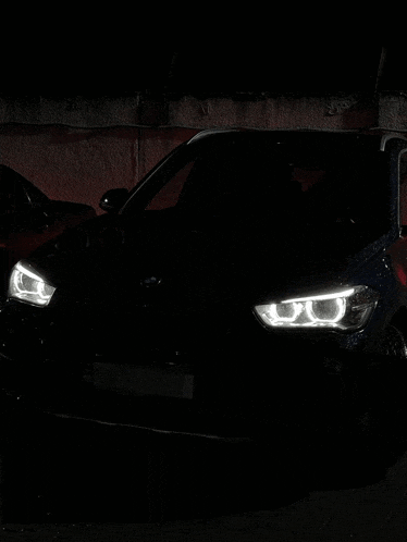 a black bmw is parked in the dark with the headlights on