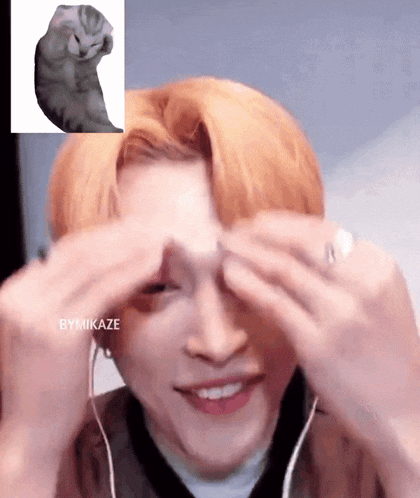 a person covering their eyes with their hands and a picture of a cat in the background