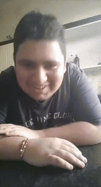 a young man wearing a shirt that says " fine clothes " sits at a table