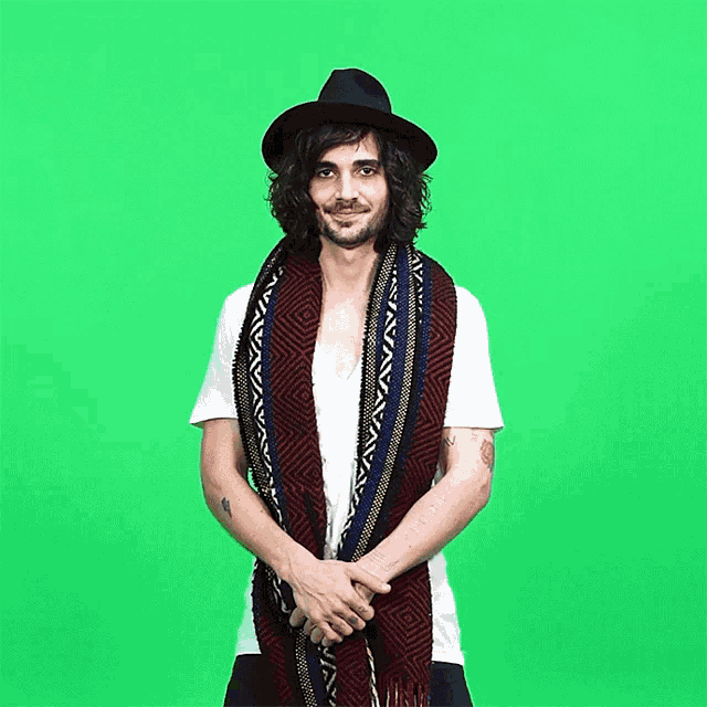 a man wearing a hat and scarf stands in front of a green background