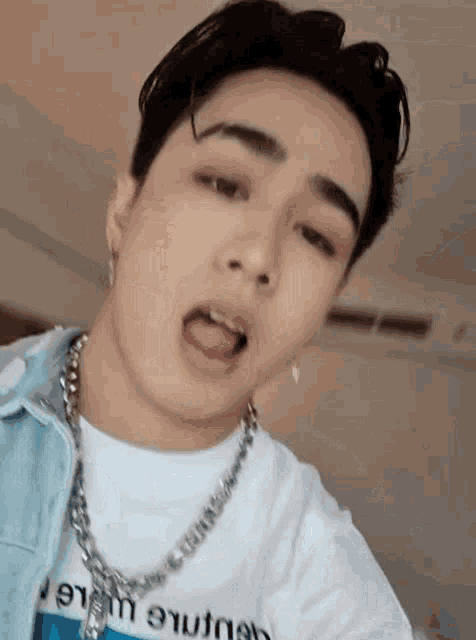 a young man wearing a denim jacket and a necklace is taking a selfie .