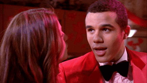 a man in a red suit and bow tie talks to a girl