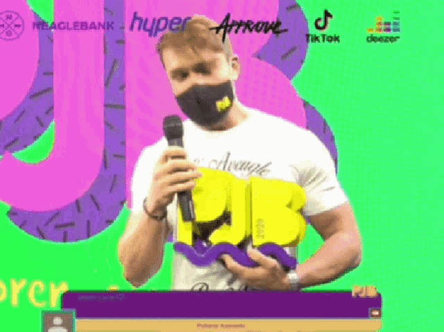 a man wearing a mask is holding a microphone in front of a green background that says hyper arrow