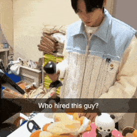 a man is standing in front of a table with a sign that says who hired this guy on it