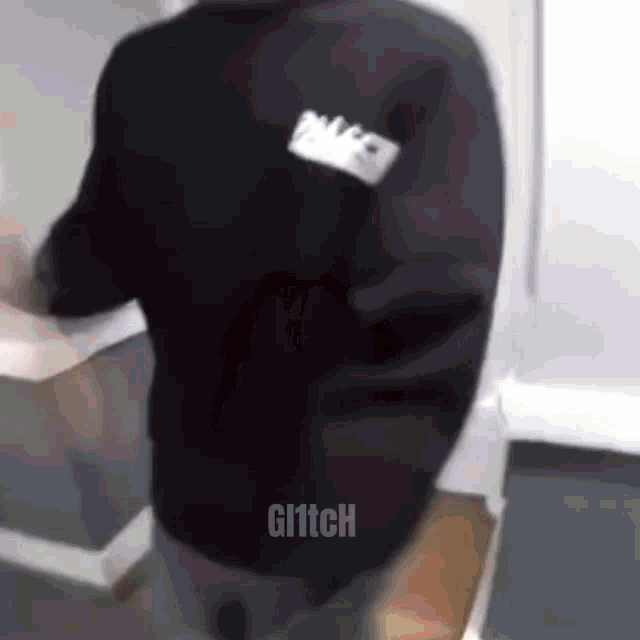 a man wearing a black sweatshirt with a name tag on the back is standing in a room .