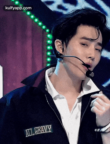 a young man wearing a jacket and a microphone is singing into it .