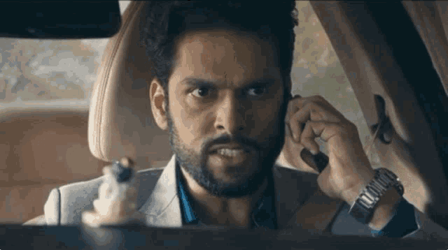 a man with a beard is driving a car and talking on a cell phone .